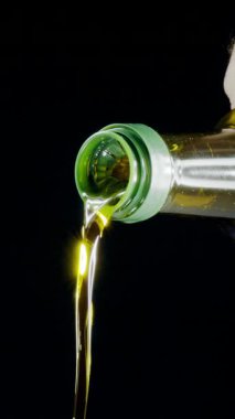 Ekstra saf zeytinyağı, siyah arka plandaki zeytinyağından dökülüyor. Yavaş çekim dikey şablonu.