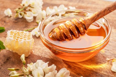 Ahşap kaşığı balla cam kaseye daldırmak, akasya çiçekleri yakındaki ahşap masada. Üst görünüm.