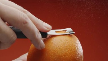 Özel bir mutfak aletiyle portakal kabuğu almak; portakal arkaplanındaki kesiğin altına gerekli yağlı portakal suyu serpiştirmek. Yavaş çekim makro video. 