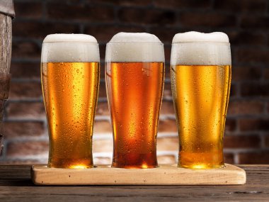 Eski ahşap masada üç bardak soğuk bira ve arka planda tuğla duvar.. 