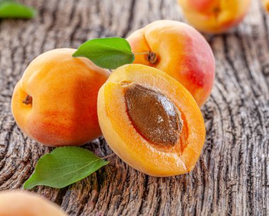 Eski ahşap masada yeşil yapraklı olgun kayısılar..