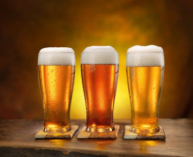 Eski ahşap masada üç bardak soğuk bira ve arka planda koyu bir duvar.. 