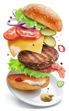 Biftek köfteli, sebzeli ve peynirli çizburger malzemeleri beyaz arka planda bir tabağın üzerinde havada yüzüyor. Dosya kırpma yolları içeriyor.