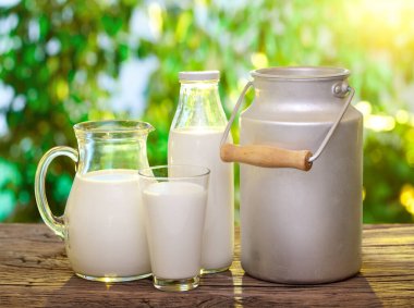 Dekan, şişe ve bir bardak süt ahşap masa ve bulanık yeşil doğa arka planı.
