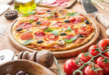 Vişneli domates, salam ve diğer malzemelerle kaplı pizza ahşap masanın üzerinde. Üst görünüm.