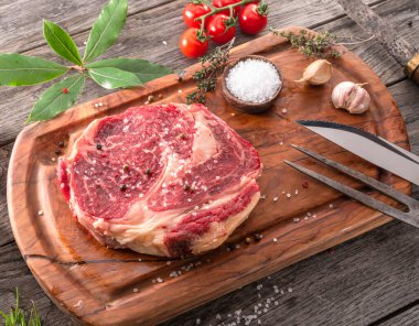 Ahşap tahtanın üzerinde çiğ biftek ve baharat var..