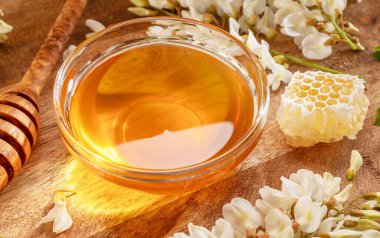 Cam kasede doğal organik bal, akasya çiçekleri ve ahşap masanın üzerinde yapraklar. Üst görünüm.