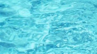 Havuzun suyunda dalgalanmalar. Şeffaf, ışıl ışıl ve hareketli suyun davetkar yüzeyi. Yukarıdan bak. Yavaş çekim ve döngülü video.