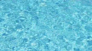 Havuzun suyunda dalgalanmalar. Şeffaf, ışıl ışıl ve hareketli suyun davetkar yüzeyi. Yukarıdan bak. Yavaş çekim ve döngülü video.