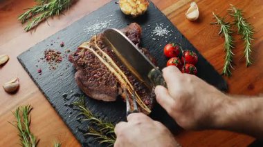 Orta pişmiş T-Bone bifteği, otlar ve sarımsak servis tahtasında yakın plan..