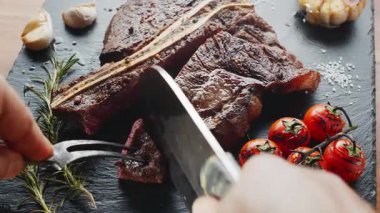 Orta pişmiş T-Bone bifteği, otlar ve sarımsak servis tahtasında yakın plan..