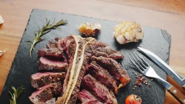 Orta pişmiş T-Bone bifteği, otlar ve sarımsak servis tahtasında yakın plan..