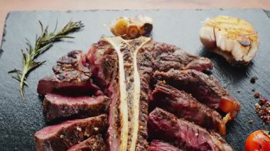 Orta pişmiş T-Bone bifteği, otlar ve sarımsak servis tahtasında yakın plan..