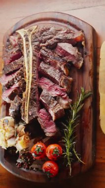 Orta pişmiş T-Bone bifteği, otlar ve sarımsak servis tahtasında yakın plan..