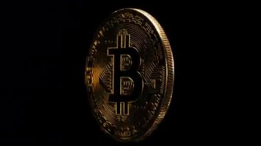 Siyah zemin üzerinde Bitcoin logosu ekseni etrafında dönen fiziksel altın kaplama sikke.