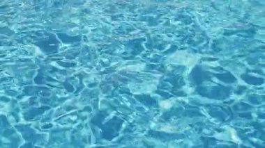 Havuzun suyunda dalgalanmalar. Şeffaf, ışıl ışıl ve hareketli suyun davetkar yüzeyi. Yukarıdan bak. Yavaş çekim ve döngülü video.