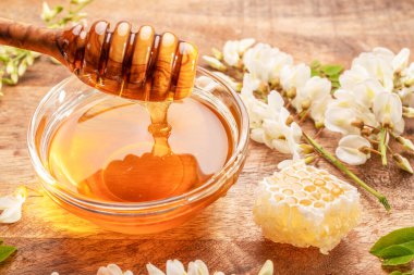 Bal, cam kasedeki tahta kaşıktan damlıyor organik bal, bal bitkisi akasya çiçekleri ve ahşap masanın yanında yapraklar. Üst görünüm.