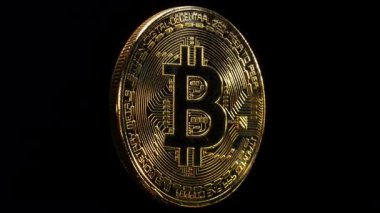 Siyah zemin üzerinde Bitcoin logosu ekseni etrafında dönen fiziksel altın kaplama sikke.