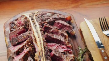 Orta pişmiş T-Bone bifteği, otlar ve sarımsak servis tahtasında yakın plan..