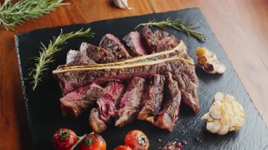 Orta pişmiş T-Bone bifteği, otlar ve sarımsak servis tahtasında yakın plan..