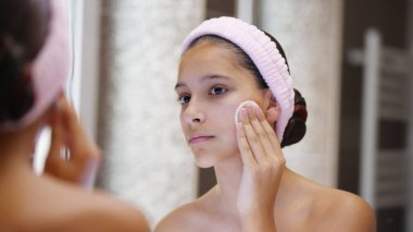 Genç kız yüzünü pamukla siliyor, makyaj malzemelerini çıkartıyor ya da makyaj yapıyor.. 