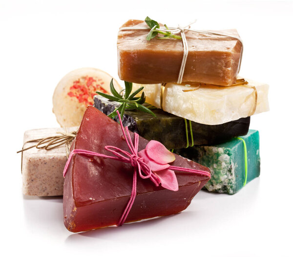 Куча разноцветного натурального мыла ручной работы и банная бомба, завязанная деревенскими нитями на белом фоне.