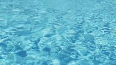 Havuzun suyunda dalgalanmalar. Şeffaf, ışıl ışıl ve hareketli suyun davetkar yüzeyi. Yukarıdan bak. Yavaş çekim ve döngülü video.