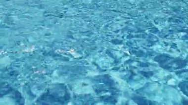 Havuzun suyunda dalgalanmalar. Şeffaf, ışıl ışıl ve hareketli suyun davetkar yüzeyi. Yukarıdan bak. Yavaş çekim ve döngülü video.