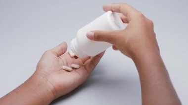Beyaz kapsüller ya da plastik şişeden açık gri arka plana dökülen haplar. İlaç, sağlık, takviye ve ilaç tedavisi kavramı.