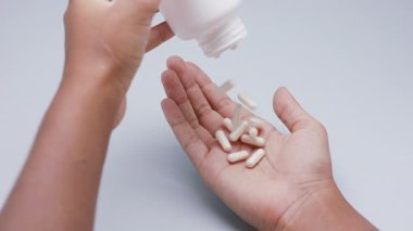Beyaz kapsüller ya da plastik şişeden açık gri arka plana dökülen haplar. İlaç, sağlık, takviye ve ilaç tedavisi kavramı.