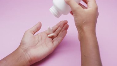 Beyaz kapsüller ya da plastik bir şişeden pembe arka plana dökülen haplar. İlaç, sağlık, takviye ve ilaç tedavisi kavramı.