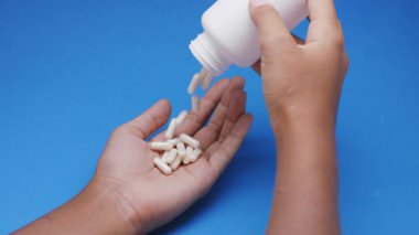 Beyaz kapsüller ya da plastik şişeden mavi arka plana dökülen haplar. İlaç, sağlık, takviye ve ilaç tedavisi kavramı.
