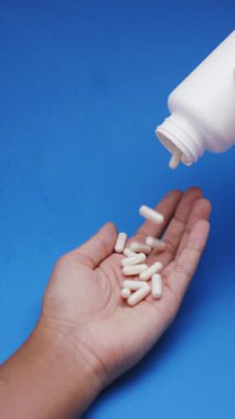 Beyaz kapsüller ya da plastik şişeden mavi arka plana dökülen haplar. İlaç, sağlık, takviye ve ilaç tedavisi kavramı.