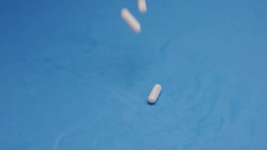 Yavaş çekim videosu: mavi arka plana düşen beyaz haplar ya da kapsüller. İlaç, sağlık, takviye ve ilaç tedavisi kavramı.