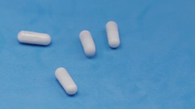 Yavaş çekim videosu: mavi arka plana düşen beyaz haplar ya da kapsüller. İlaç, sağlık, takviye ve ilaç tedavisi kavramı.