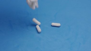 Yavaş çekim videosu: mavi arka plana düşen beyaz haplar ya da kapsüller. İlaç, sağlık, takviye ve ilaç tedavisi kavramı.