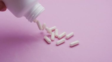 Yavaş çekim videosu: Pembe arka plana düşen beyaz haplar veya kapsüller. İlaç, sağlık, takviye ve ilaç tedavisi kavramı.