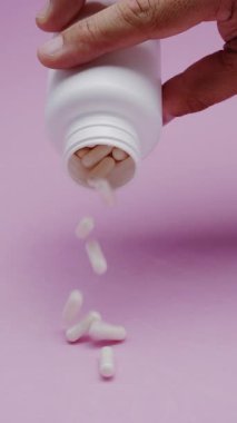 Yavaş çekim videosu: Pembe arka plana düşen beyaz haplar veya kapsüller. İlaç, sağlık, takviye ve ilaç tedavisi kavramı.