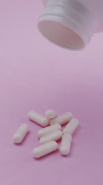 Yavaş çekim videosu: Pembe arka plana düşen beyaz haplar veya kapsüller. İlaç, sağlık, takviye ve ilaç tedavisi kavramı.