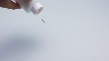 Masadaki plastik şişeden beyaz kapsüller ya da haplar dökülüyor..