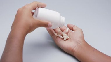 Beyaz kapsüller ya da plastik şişeden açık gri arka plana dökülen haplar. İlaç, sağlık, takviye ve ilaç tedavisi kavramı.