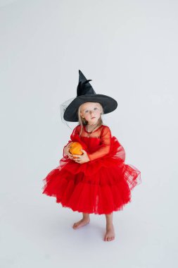 Sivri uçlu şapkalı küçük bir cadı balkabağı tutuyor. Cadılar Bayramı kostümlü bir çocuk mutlu bir şekilde gülümsüyor. Çocuk tatili. beyaz izole arkaplan.