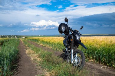 Kırsal yolda altın buğday tarlasının önünde bir motosiklet.