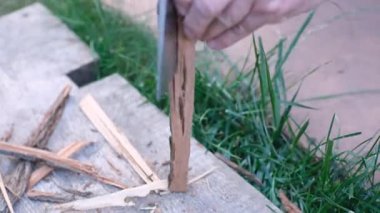 Adamın eli balta bıçağıyla şenlik ateşi için odun kırıntıları yapıyor.