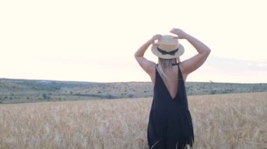 Siyah elbiseli ve şapkalı mutlu orta yaşlı kadın gün batımında buğday tarlasında koşuyor.