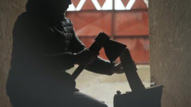 Aşağı ceketli adam ahır ortamında siluet görünümlü odun kesiyor.