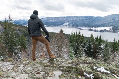 Dağın tepesinde bir fotoğrafçı gölün ve kış ormanının fotoğraflarını çekiyor.