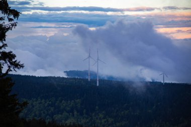 Dağdaki rüzgar türbinlerinin destansı görüntüsü alçak bulutlar ve sis