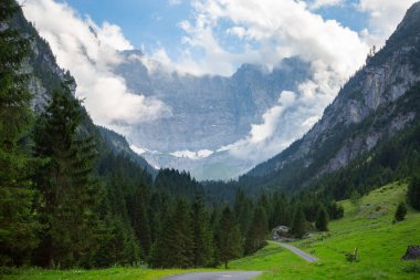 Orman vadisiyle çevrili bulutların arasındaki dağ duvarının destansı manzarası. Yürüyüş ve seyahat kavramı