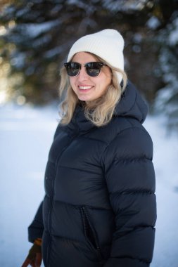 Siyah ceketli orta yaşlı beyaz kadın ve karlı ormanda güneş gözlüğü.
